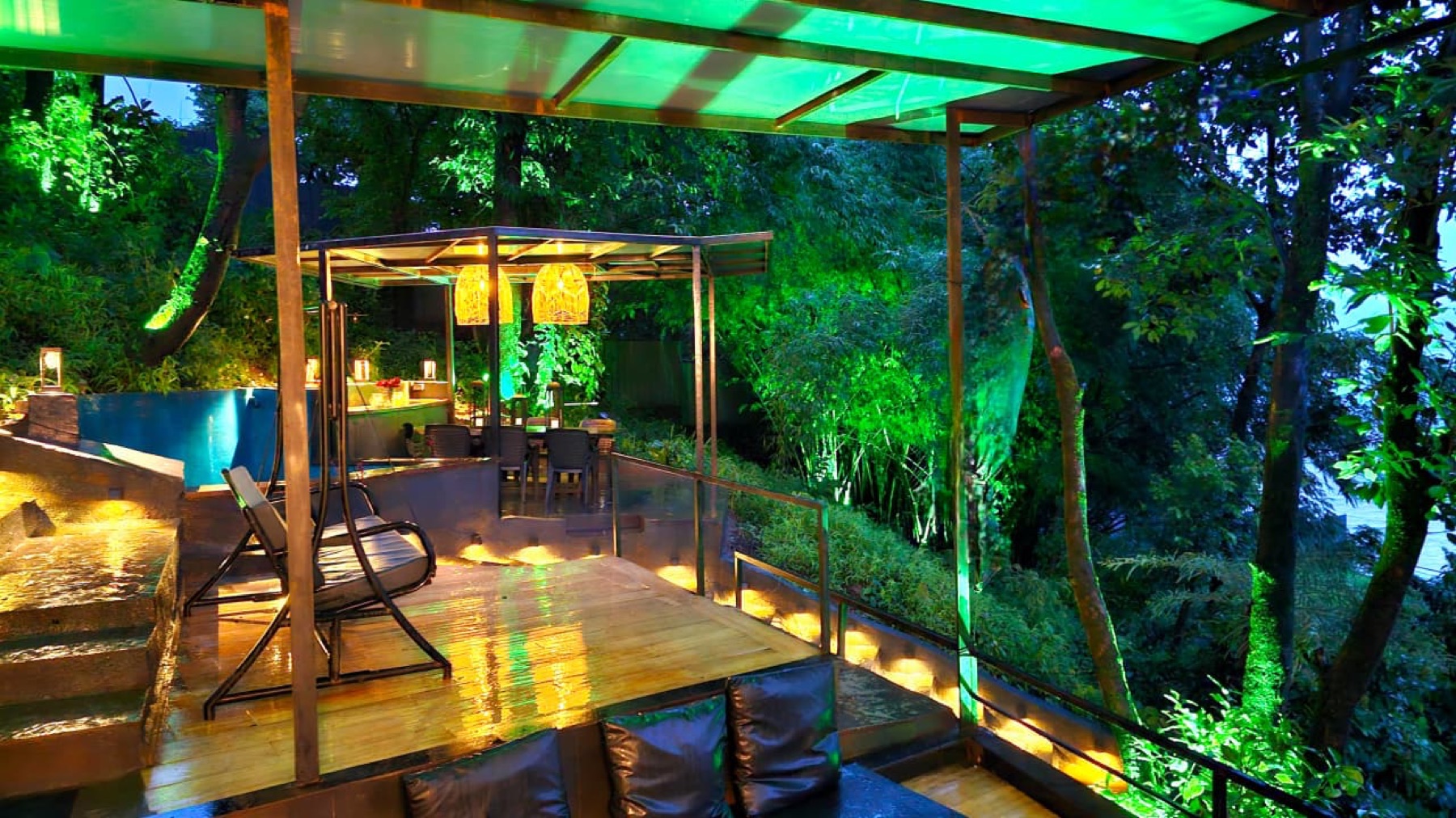 Timber dining deck under a lit pergola surrounded by dense green foliage