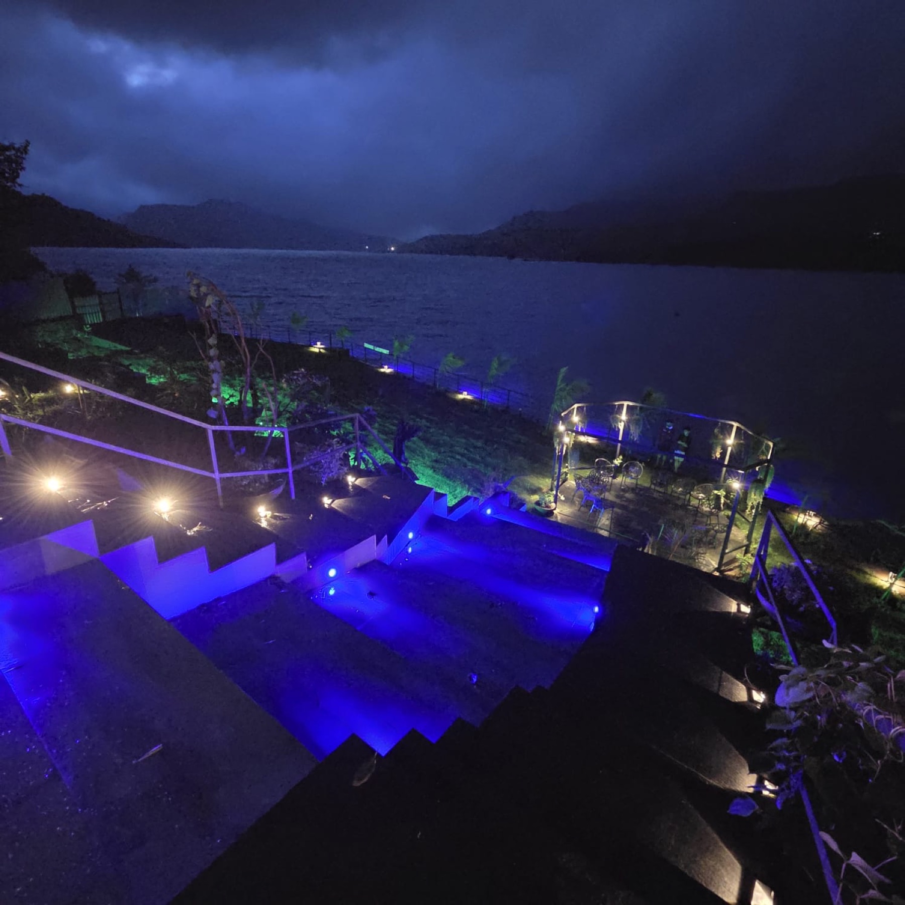 The lit basalt terraces of Nirvana Lakefront stepping down to the dark lake at night