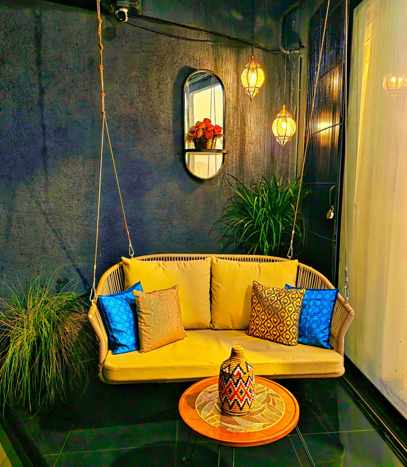 A hanging swing seat with blue and gold cushions under Moroccan lanterns