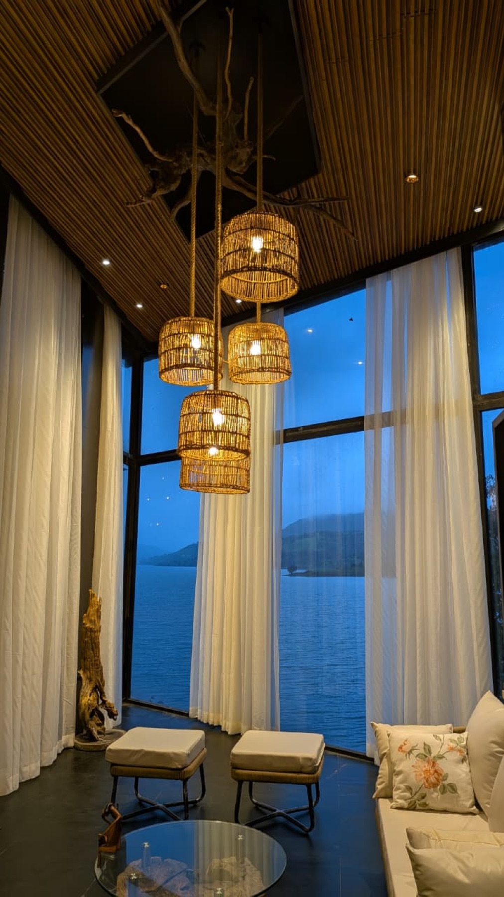Cane pendant lights hanging in the double-height glass living room with the lake beyond at blue hour